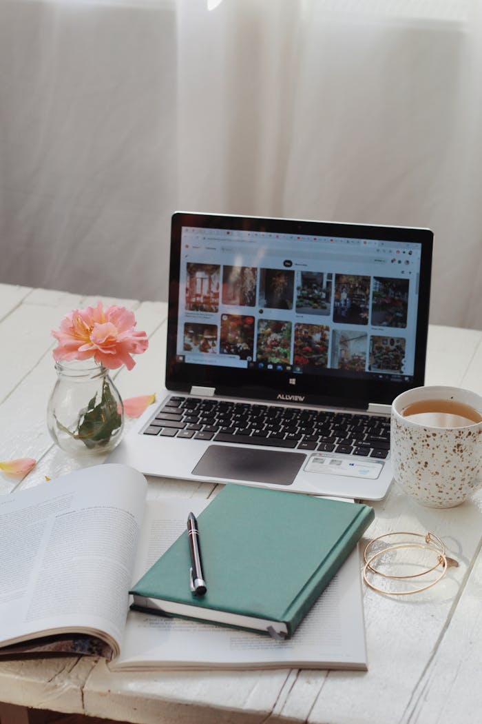 A laptop with open planner and coffee cup on a white desk, creating a cozy workspace.